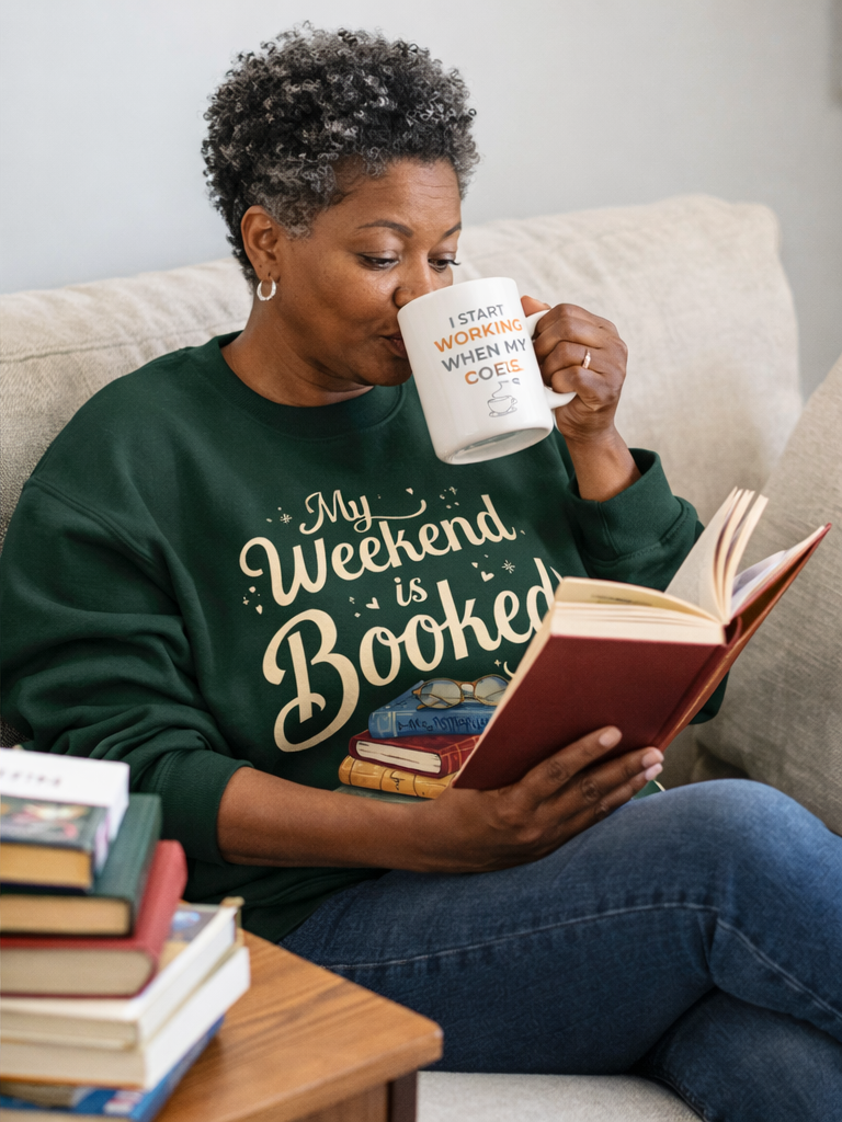 Woman sitting on a couch reading a book and holding a mug with text.